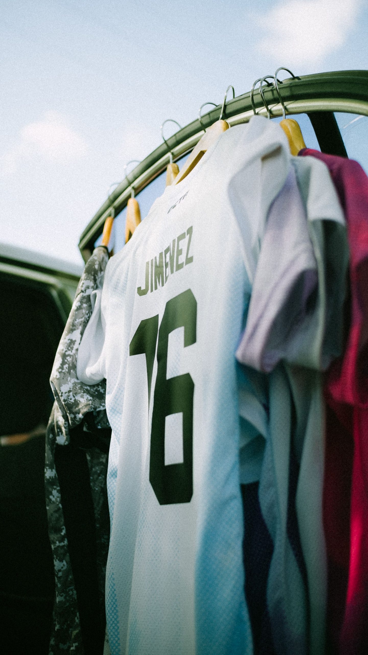 A white soccer jersey with the number 16 hangs among colorful clothes on a rack.