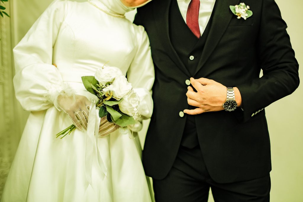 Elegant couple in black suit and white dress on their wedding day, holding hands and flowers.