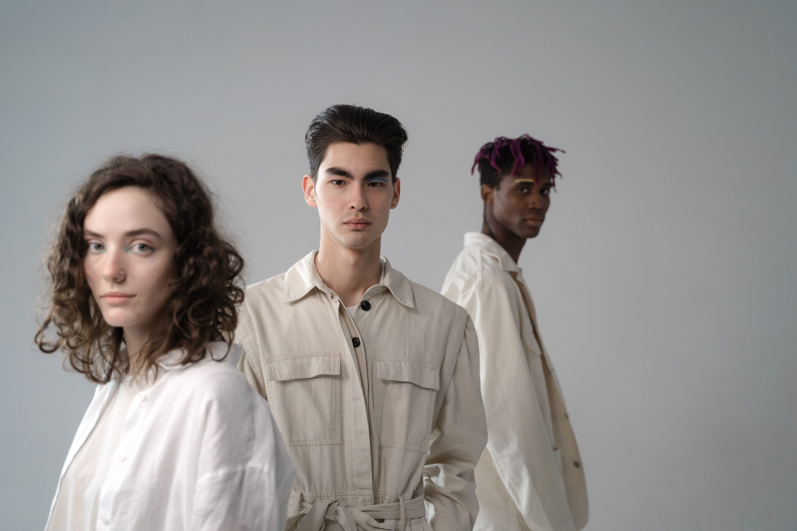 Group of diverse multiethnic young people wearing light beige and white cotton clothes standing in studio and looking at camera on gray background